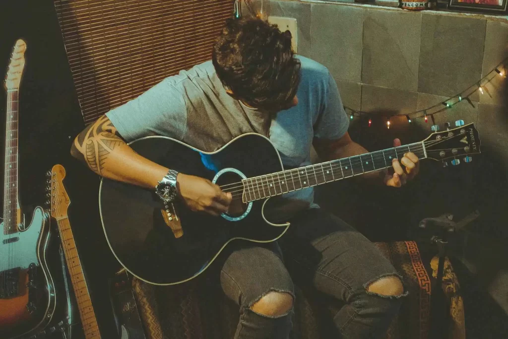 a young man playing a black acoustic guitar